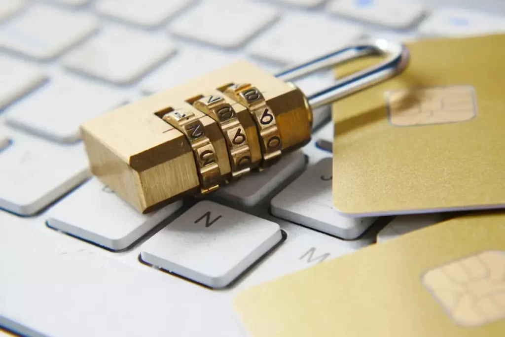 A brass combination padlock on a laptop keyboard next to gold coloured bank cards