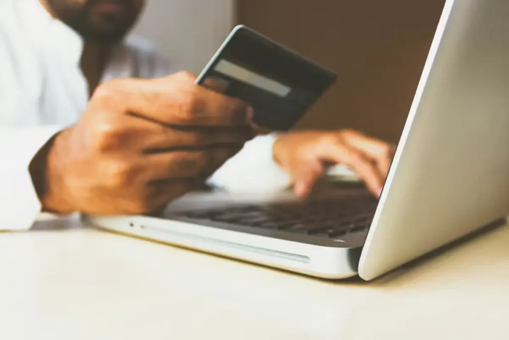 A man holding a bank card while typing on a laptop to make an online purchase