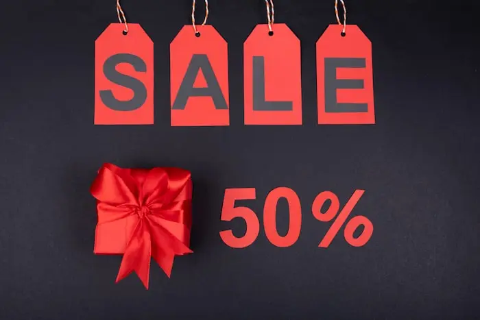 Punased hinnasildid kirjaga „SALE” ja 50% allahindlus kinkekarbi kõrval mustal taustal