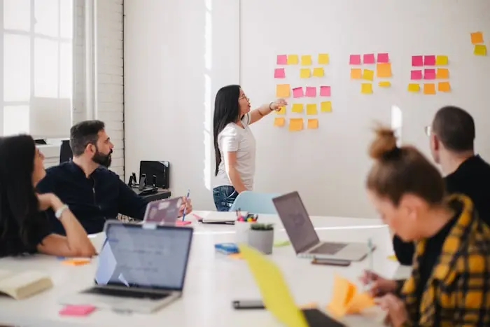 Team meeting in the office; a woman is presenting ideas on the wall using colorful sticky notes