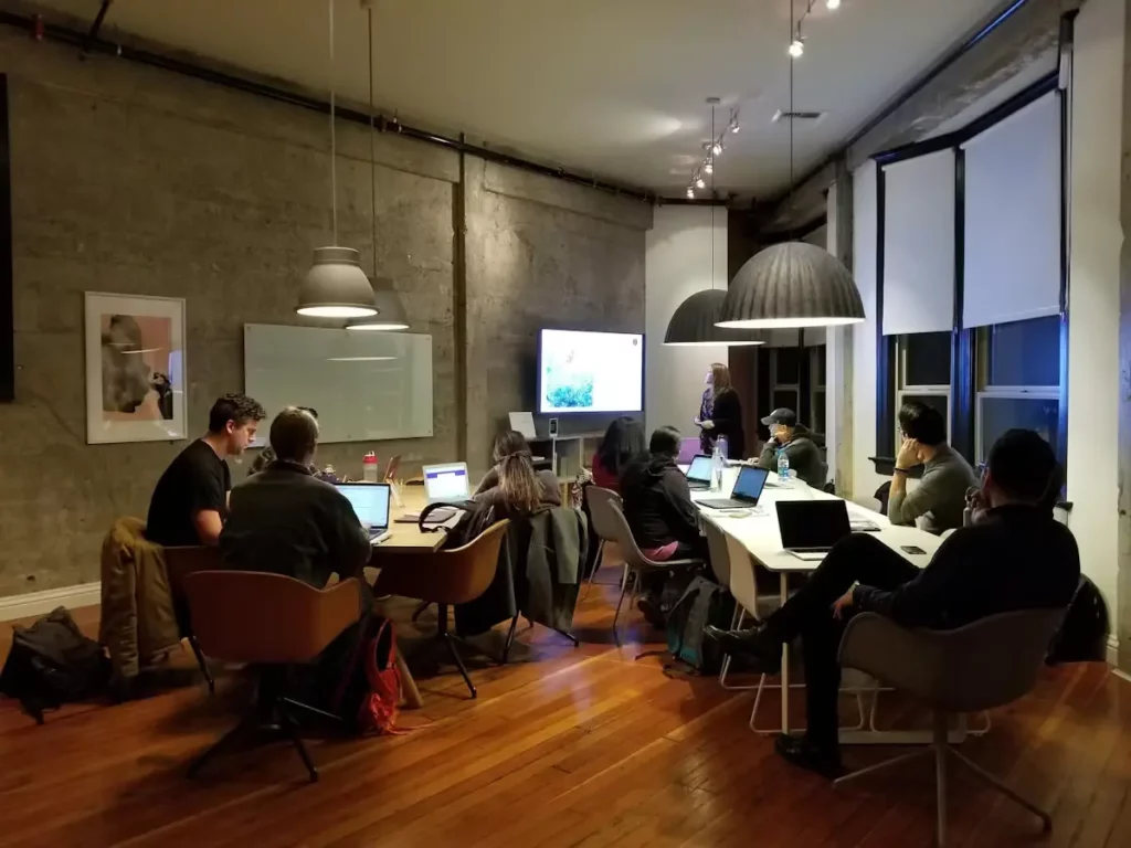 A group of people at a training event in a loft style office watching a presentation on a screen